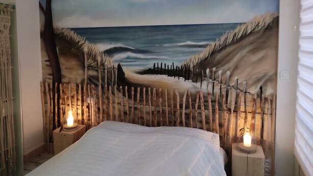Une chambre à coucher avec une fresque représentant une scène de plage, un lit et deux lampes de chevet.