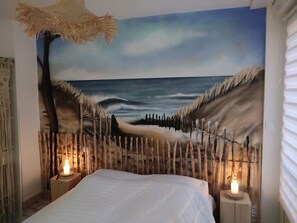 Une chambre à coucher avec une fresque représentant une scène de plage, un lit et deux lampes de chevet.