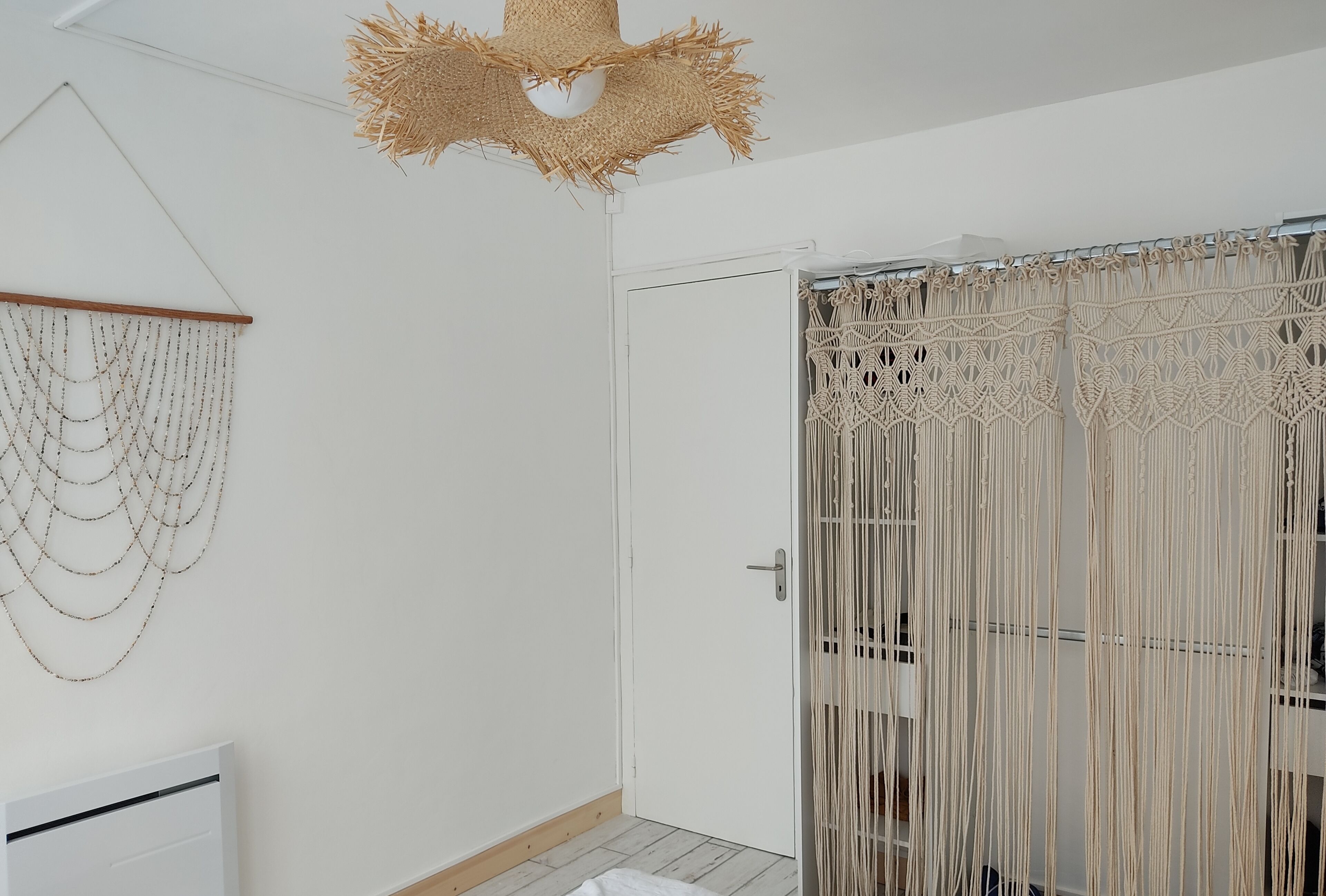 A room with a macramé curtain, a wall hanging, and a ceiling light fixture.