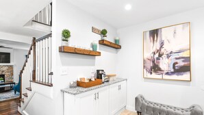 Cozinha moderna com armários brancos, prateleiras de madeira e um banco.