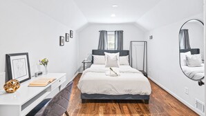 Quarto com cama, mesa de cabeceira e escrivaninha com cadeira.