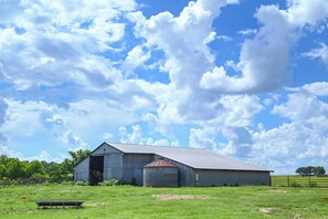 Une grande grange dotée d’un toit en métal et d’une tour à grain attenante, située dans un champ verdoyant sous un ciel dégagé.