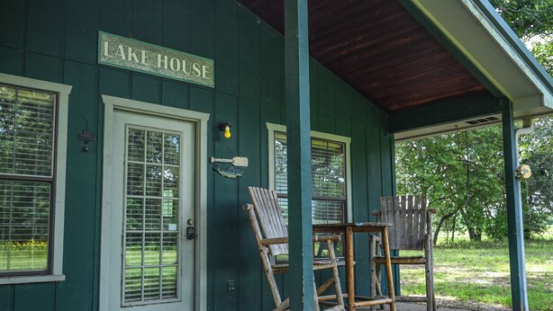 A green building labeled "LAKE HOUSE" with large windows, a covered porch, and outdoor seating. - Longhorn Lake House - Arcridgeranchresort.com (Ben Wheeler)