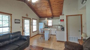 A spacious living room with a black leather couch, a wooden coffee table, and a kitchen area with white cabinets and a refrigerator. - Longhorn Lake House - Arcridgeranchresort.com (Ben Wheeler)