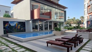 Un bâtiment moderne doté d’une façade en verre, d’une piscine et d’un espace extérieur aménagé pour s’asseoir.