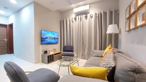 Un salon moderne avec un canapé gris, une table basse en verre et un téléviseur fixé au mur.