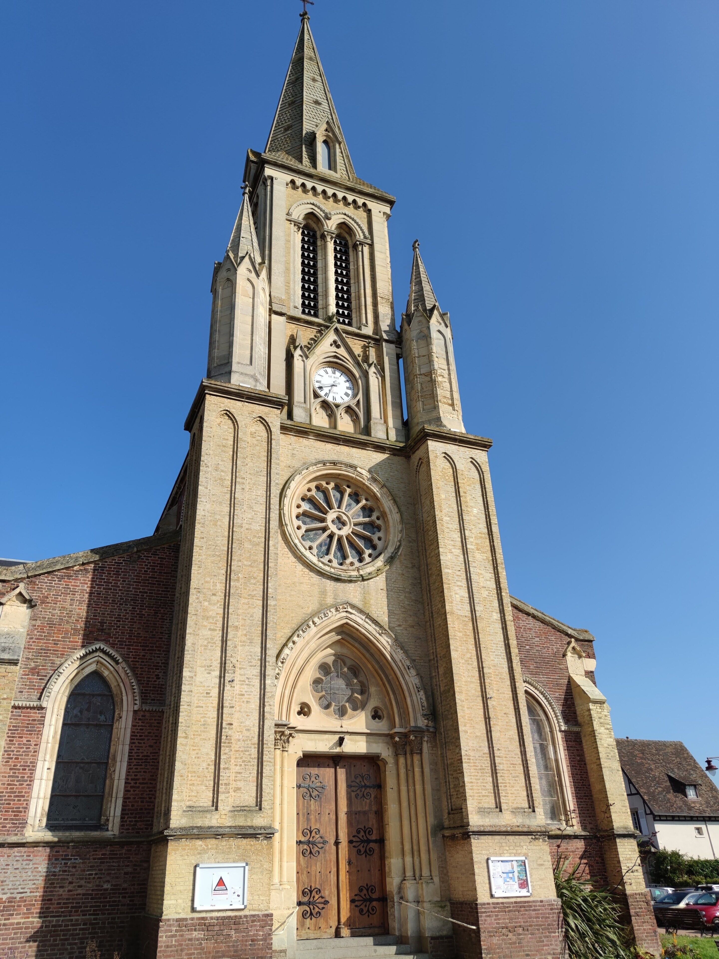 Una iglesia con un campanario alto, un reloj grande y una puerta de madera.