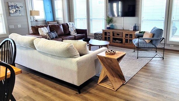 A living room with a sofa, coffee table, and a TV mounted on the wall. - 3 BR/3 BA Village Walk House, Close to the Beach, Community Pool! (Port Aransas)
