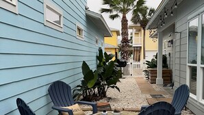 A patio with four blue chairs and a small round table, surrounded by pebbles. - 3 BR/3 BA Village Walk House, Close to the Beach, Community Pool! (Port Aransas)