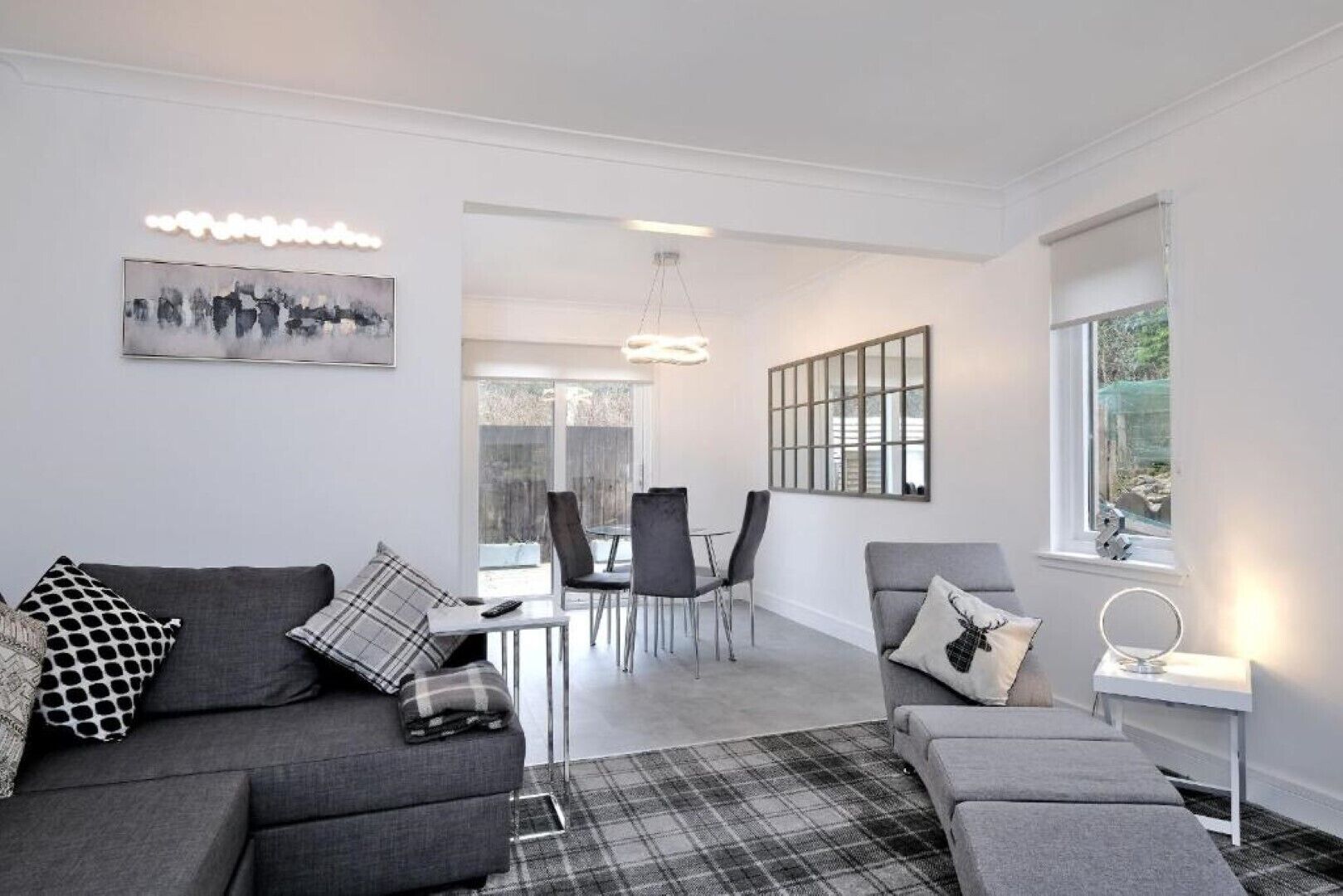 A modern living room with a grey sofa set, a dining area with chairs and a table, and a large window with a view.