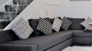 A modern living room with a grey sectional sofa, patterned cushions, a white furry rug, and a staircase with glass railings. - Contemporary HIGHLAND HOUSE close to town and Ben Nevis (Fort William)