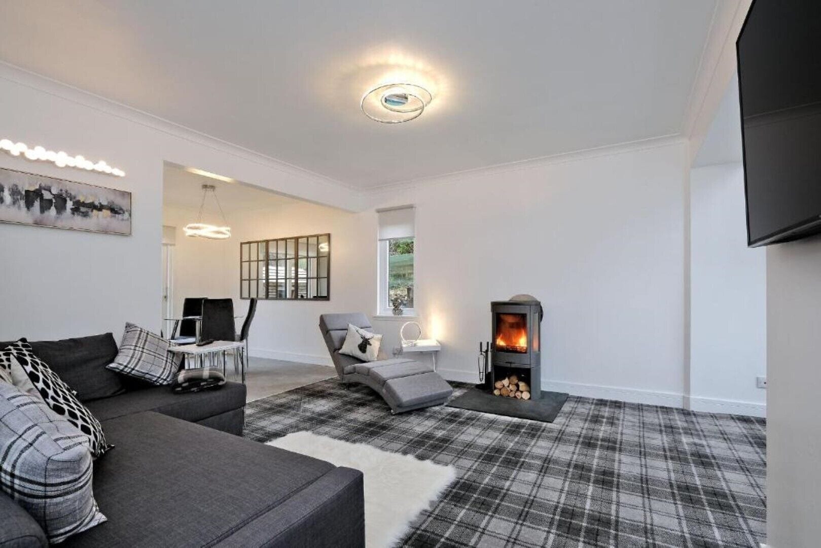 A modern living room with a fireplace, grey sofas, a plaid rug, and a minimalist design.