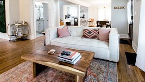 Una sala moderna con un sofá blanco, una mesa de centro de madera con libros y una alfombra estampada.