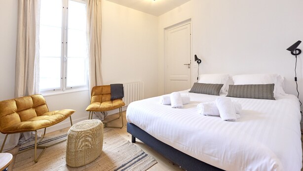 A hotel room with a large bed, two chairs, a small table, and a window with curtains. - The Yellow Nest, Studio at Victoire Square (Burdeos)