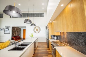 A modern kitchen with a central island, pendant lighting, and a decorative wall clock. - Seven Islands (Airlie Beach)