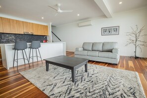A modern living space with a kitchen, a grey sofa, a coffee table, and a staircase. - Seven Islands (Airlie Beach)