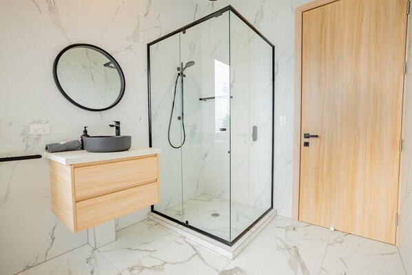 A modern bathroom with a glass-enclosed shower, a wooden vanity with a sink, and a marble-tiled floor. - Seven Islands (Airlie Beach)