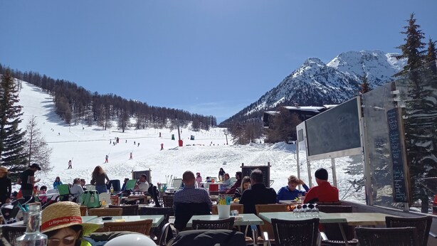 Un restaurant avec une terrasse offrant une vue sur une piste de ski enneigée.