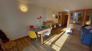 Un salon chaleureux avec un plancher en bois, un coin repas avec une table et des chaises, et un canapé bleu.