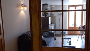 Une chambre avec un lit, une fenêtre donnant sur la cuisine et la salle à manger, et une lampe fixée au mur.