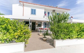 A two-story building with a patio area featuring a table and chairs, surrounded by greenery and cacti. - Beach front apartment in Marina di Ragusa (Marina di Ragusa)