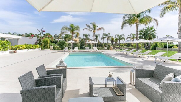 Zona junto a la piscina con sillones, sombrillas y vista despejada al agua.