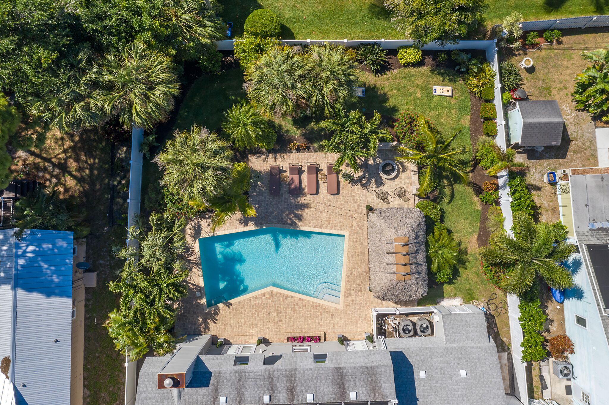 An aerial view of a residential property with a swimming pool, palm trees, and a barbecue area.