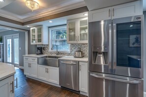 A modern kitchen with stainless steel appliances, white cabinetry, and a large window providing natural light.