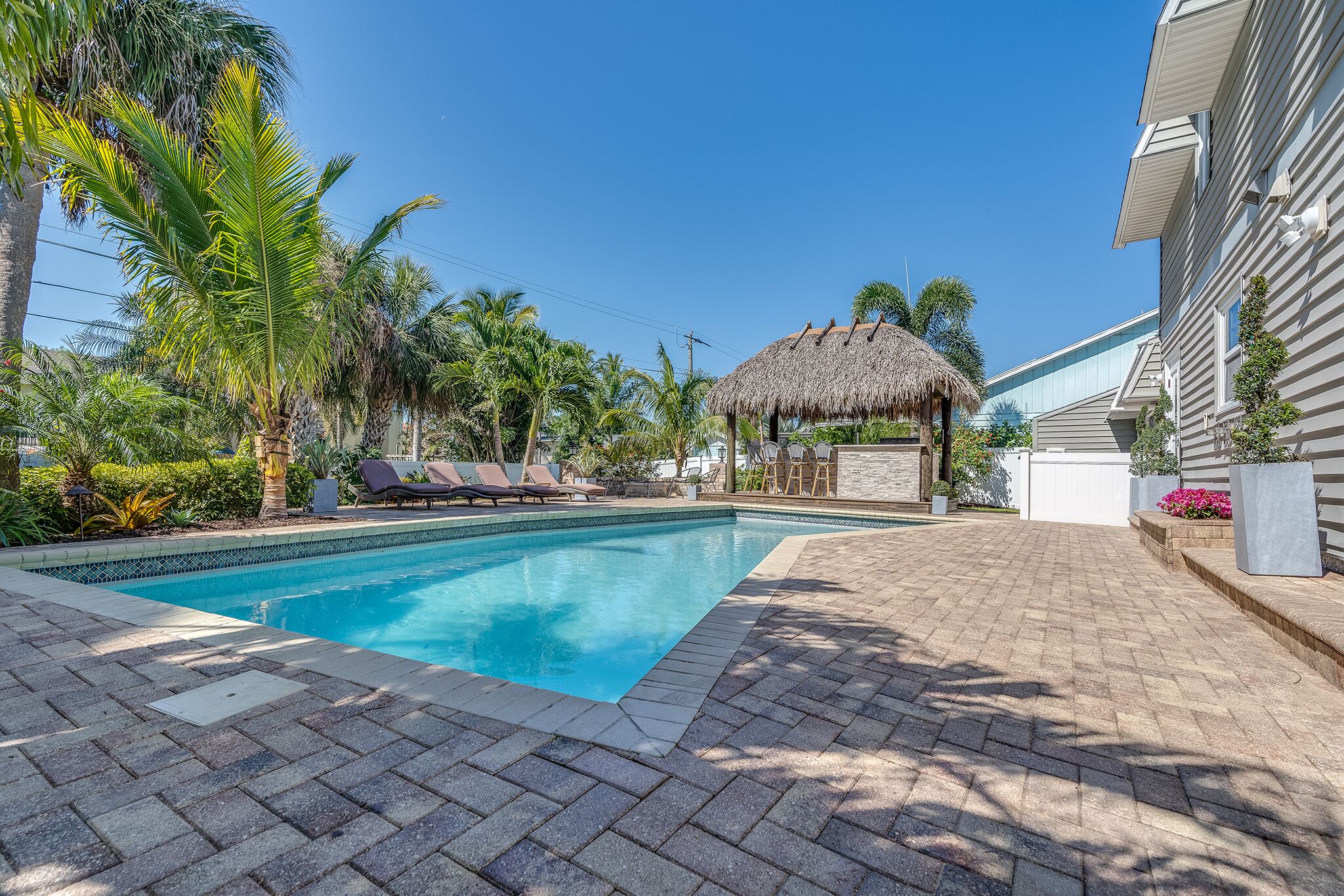 A swimming pool with lounge chairs, a thatched-roof structure, and palm trees.