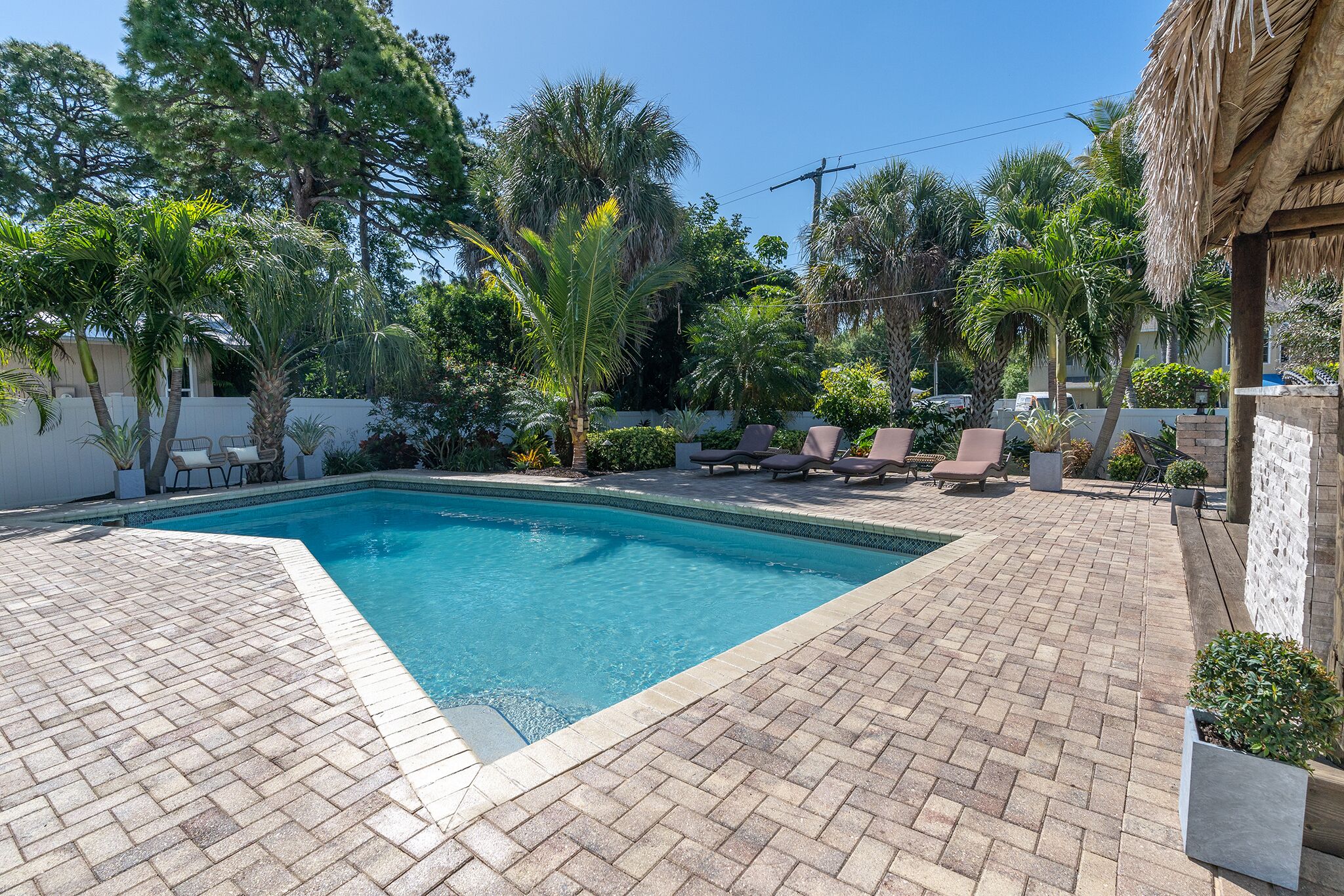 A rectangular swimming pool with a tiled edge, surrounded by a brick patio.