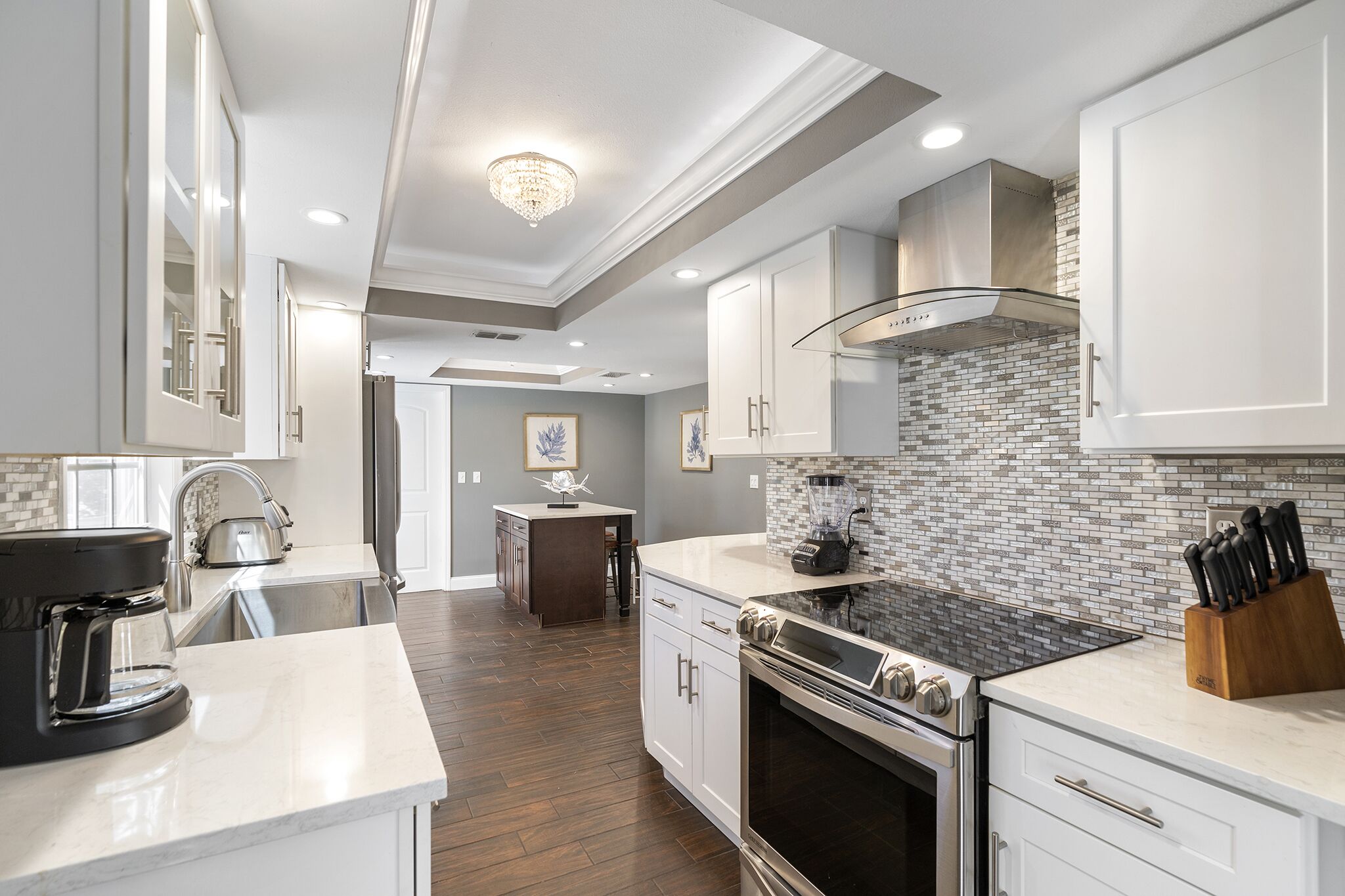 A modern kitchen with white cabinetry, a black stove, and a coffee maker.