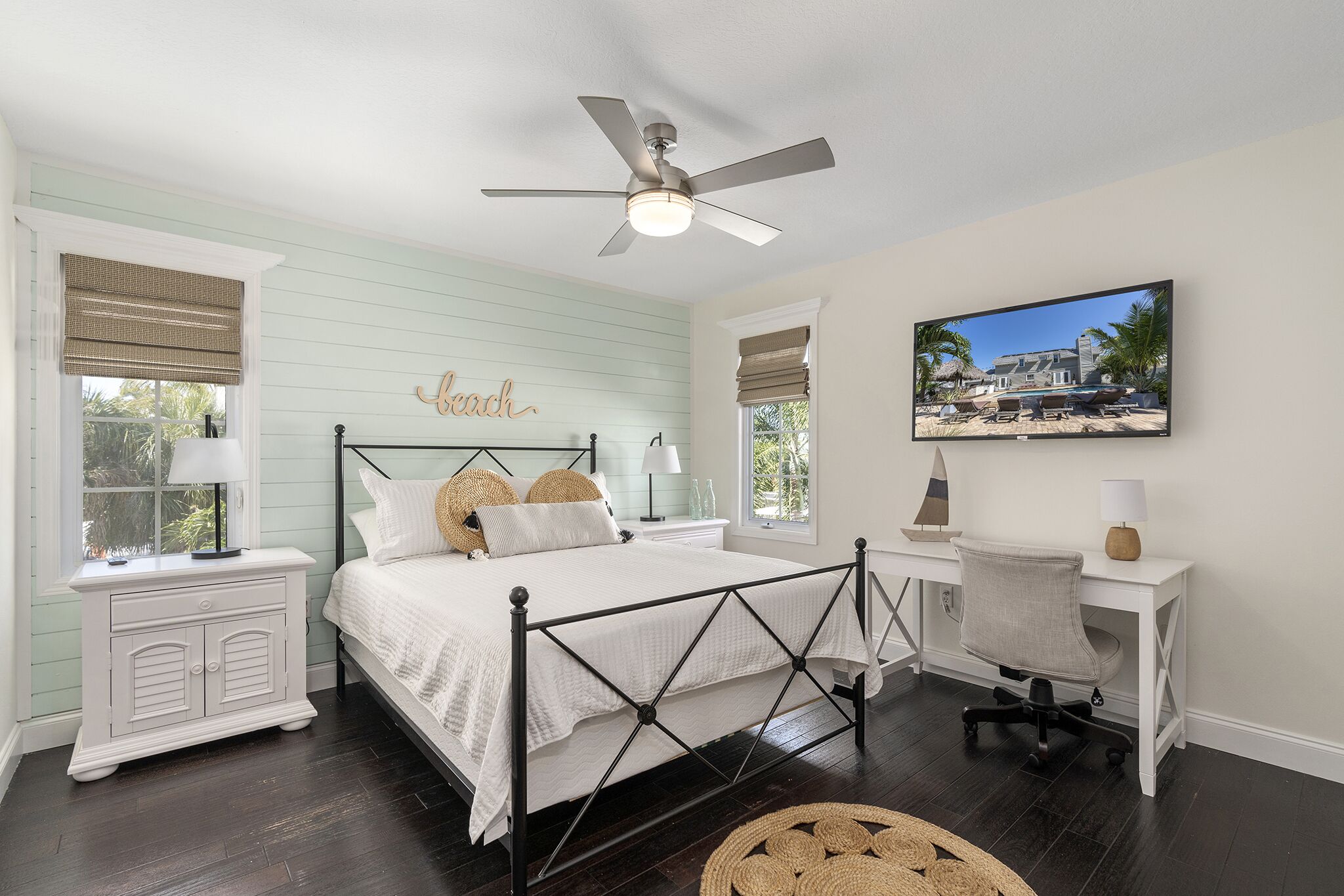 A bedroom with a bed, bedside tables, a desk, a chair, a ceiling fan, and a wall-mounted picture.
