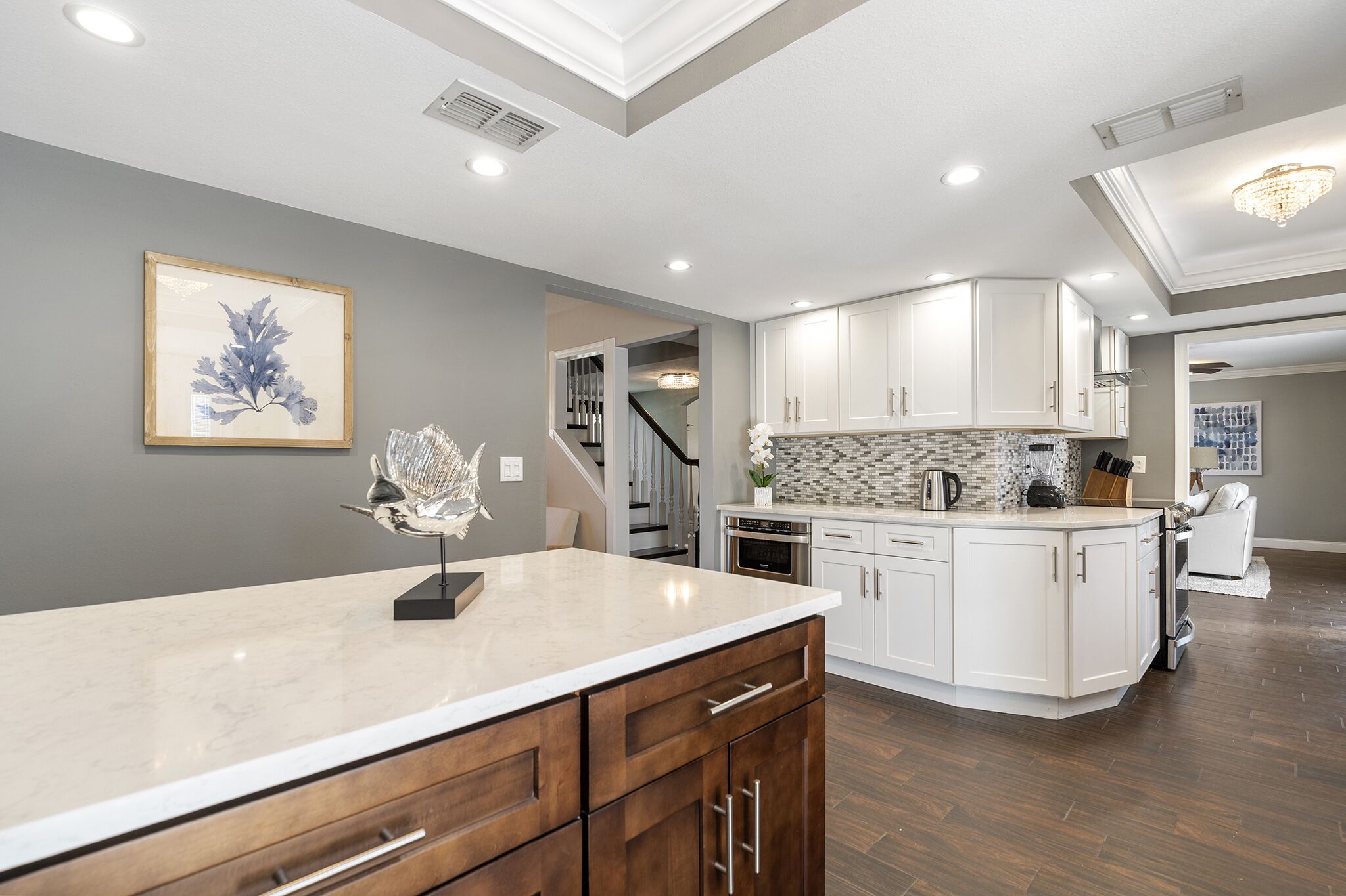 A modern kitchen with white cabinets, a marble countertop, and a staircase leading to another level.