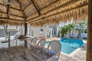 A covered outdoor area with a pool, seating, and a grill.