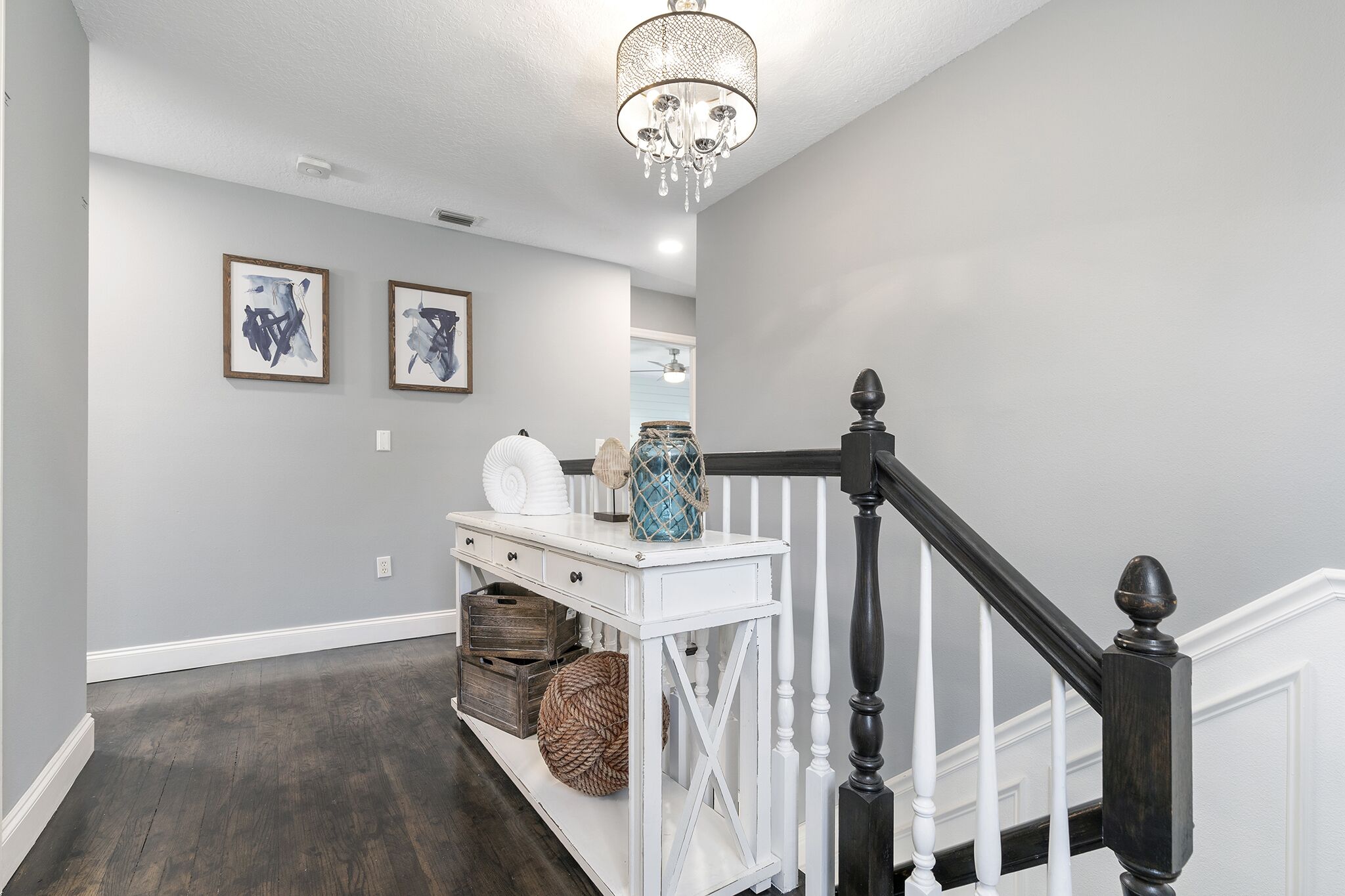 A hallway with a white console table, a chandelier, and a staircase with white railings and a dark balustrade.