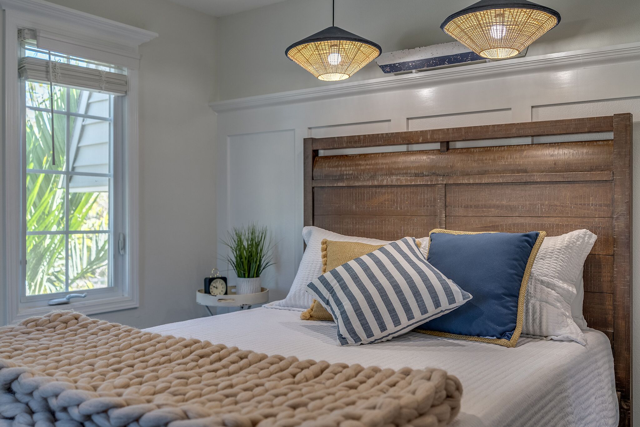 Un dormitorio con cabecera de madera, una cama grande con muchos almohadones y dos lámparas colgantes.