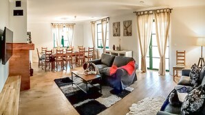 A spacious living room with a dining area, a sofa, and a TV mounted on the wall.