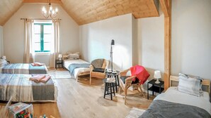 A cozy bedroom with wooden beams, two beds, a chair, a table, and a window with curtains.