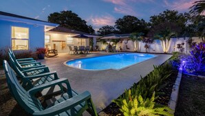 A swimming pool with lounge chairs, a covered seating area, and a well-lit patio. - Coastal Vibe • Private Heated Pool • Hot Tub • Near Beaches (Clearwater)