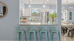 A modern kitchen with a central island, bar stools, pendant lighting, and a view of the dining area. - Coastal Vibe • Private Heated Pool • Hot Tub • Near Beaches (Clearwater)