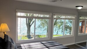 A bedroom with large windows, a bed, and a lamp.