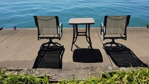 Two chairs and a small table on a concrete platform overlooking a body of water.