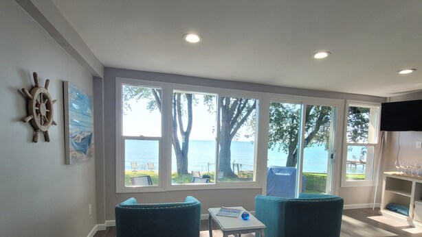 A living room with large windows, a sail wheel decoration, and a view of the sea.