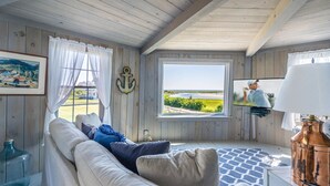 Une pièce confortable avec un plafond en bois, une grande fenêtre donnant sur la mer, une télévision et un coin salon agrémenté de coussins.