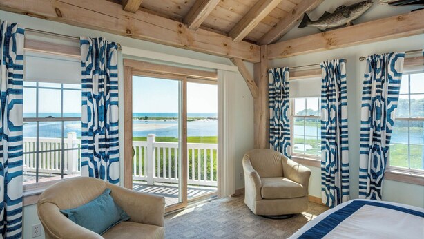 Une pièce avec une grande fenêtre, une chaise, un lit et une vue sur la plage.