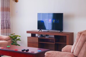 Ein Wohnzimmer mit Flachbildfernseher auf Holzständer, Couchtisch mit Fernbedienungen und einer Pflanze.