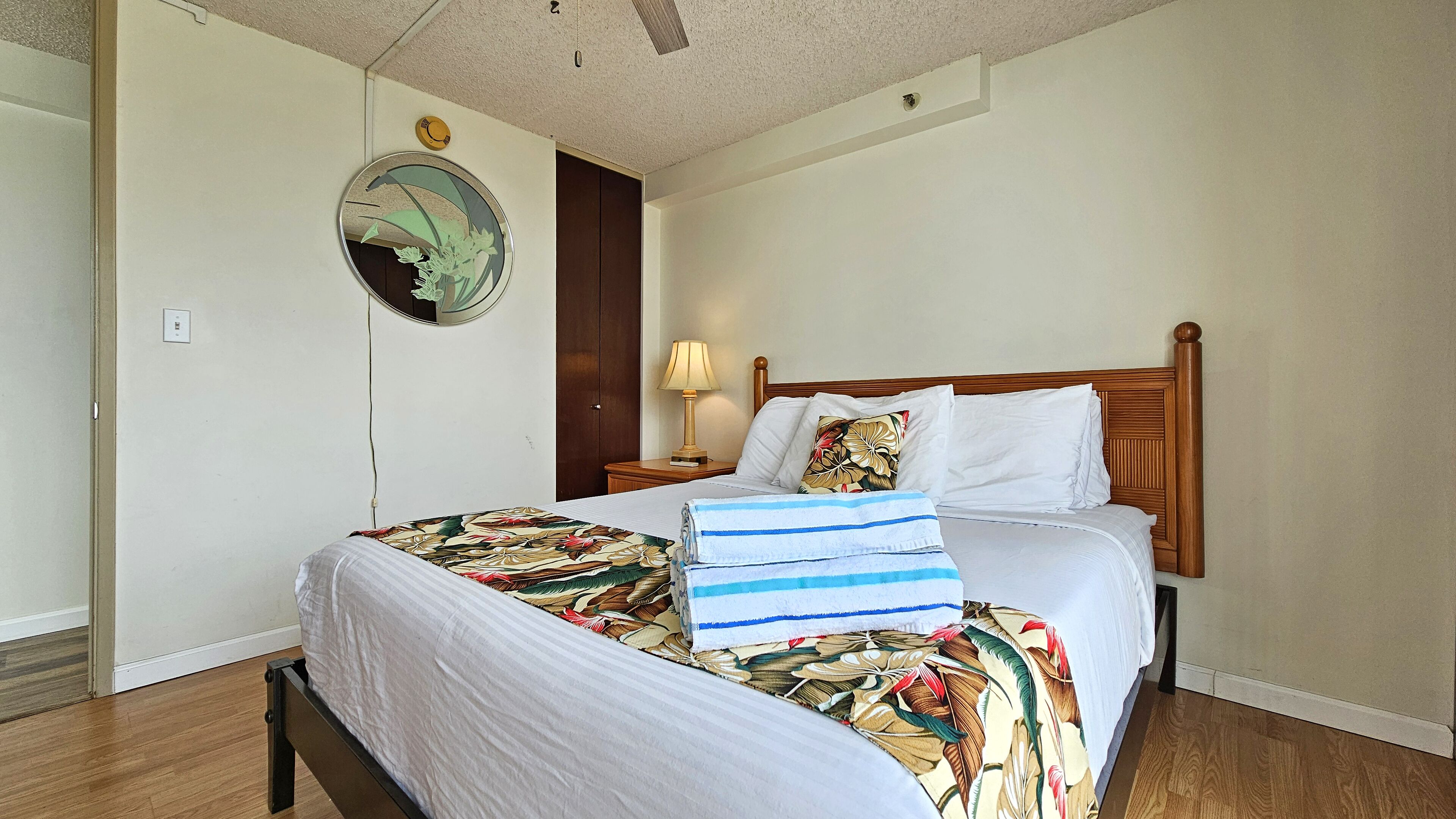A neatly made bed with floral bedding, a wooden headboard, and a bedside lamp.