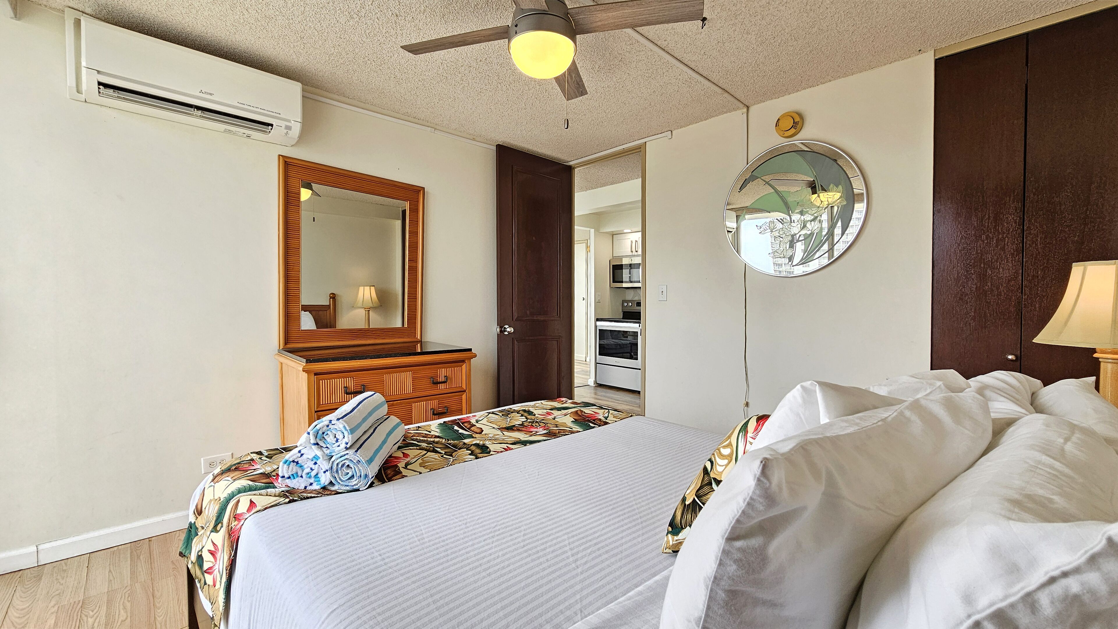 A hotel room with a bed, a dresser, a mirror, and a ceiling fan.