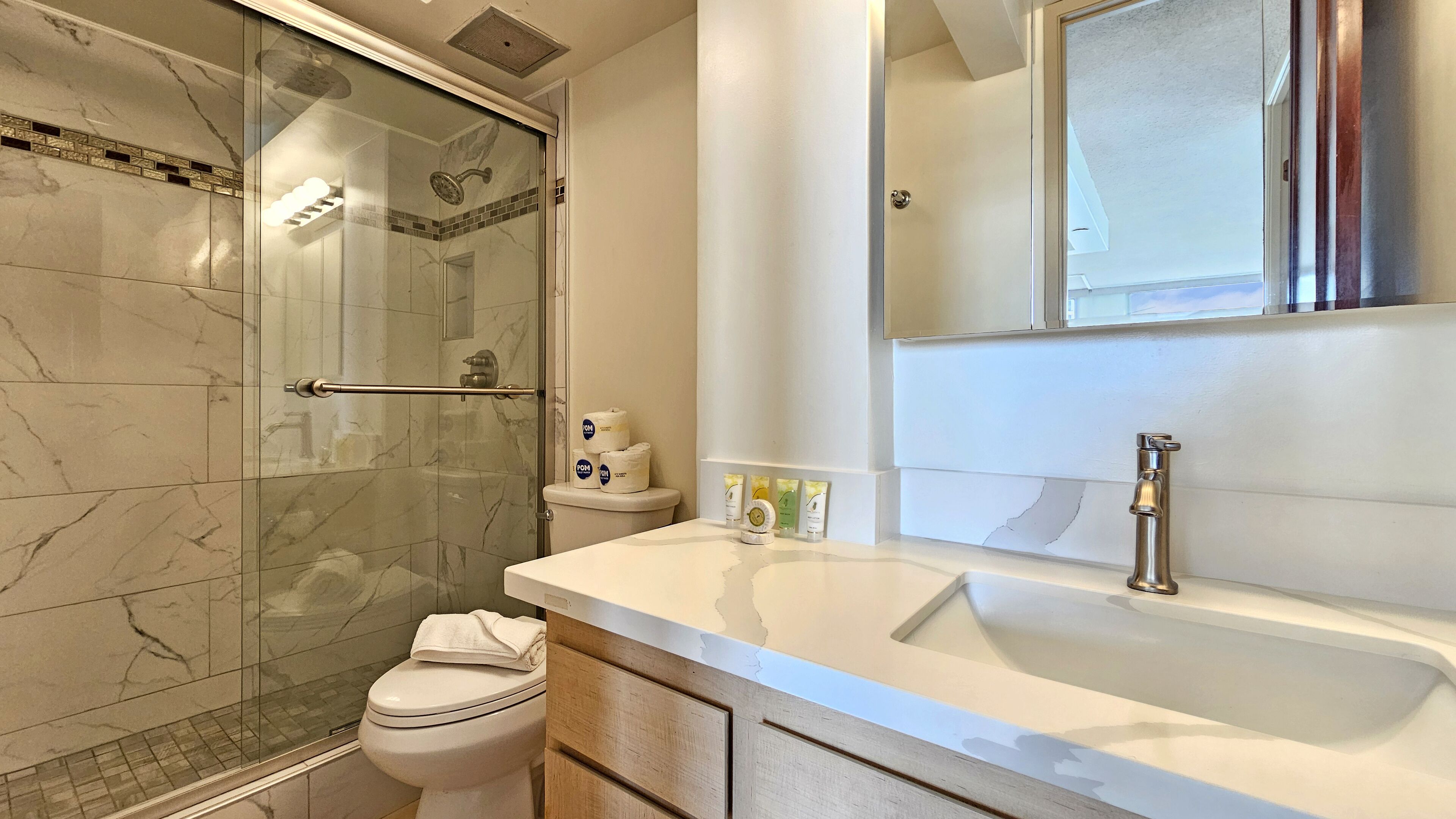Een badkamer met een douchecabine van glas, een toilet, een wastafel met spiegel en toiletartikelen op het aanrecht.