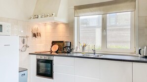 Una cocina moderna con armarios blancos, horno empotrado, cafetera y ventana con persianas.